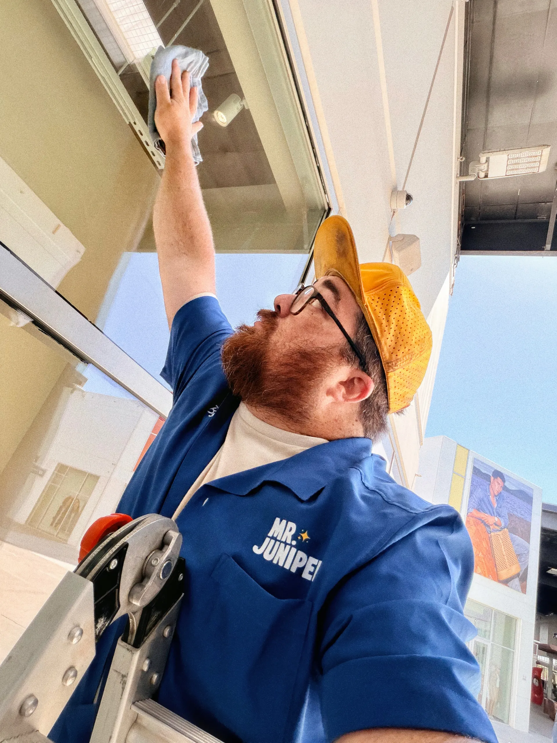 Mr. Juniper technician cleaning a storefront window with detailed attention to the glass
