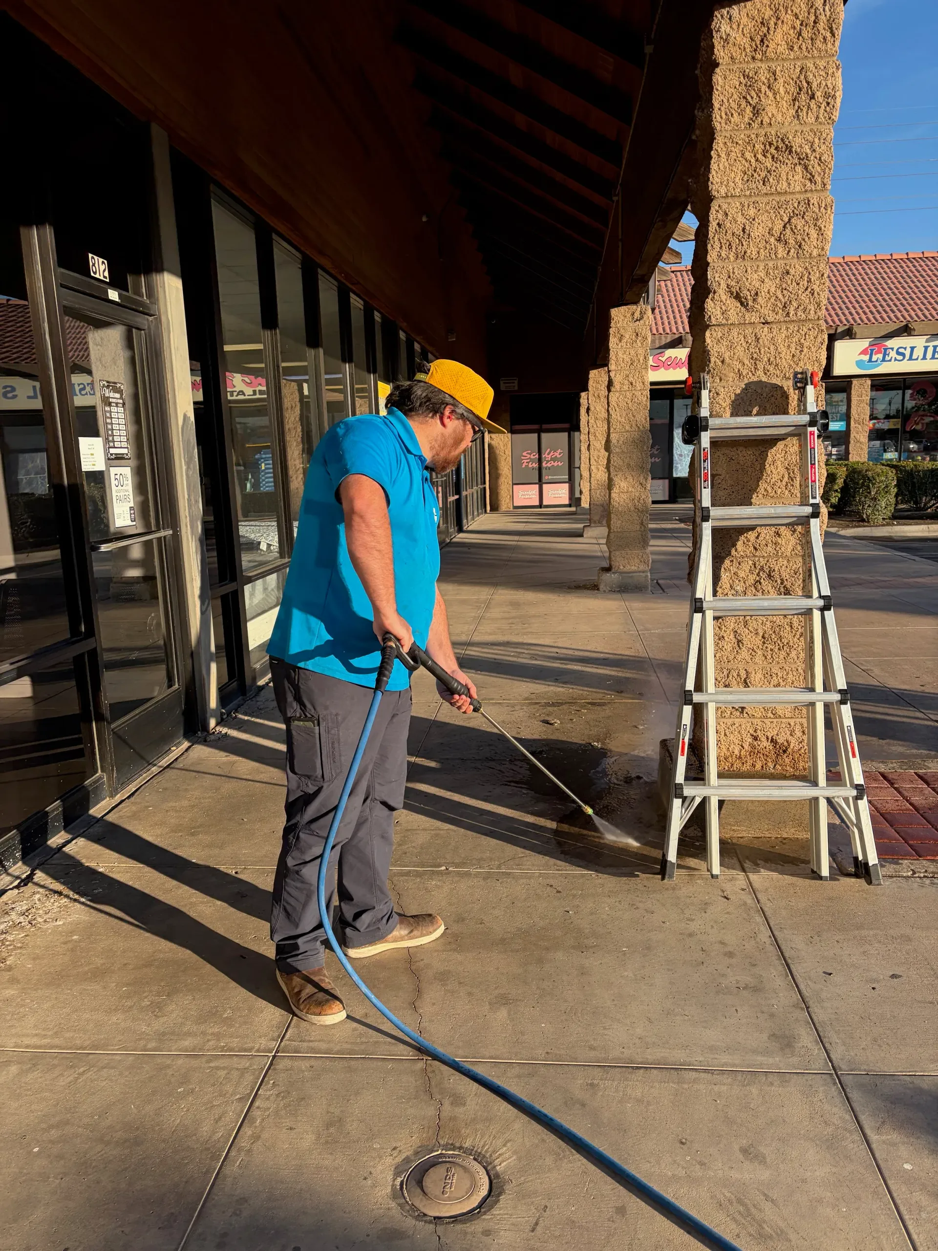 Technician pressure washing a commercial sidewalk near a storefront